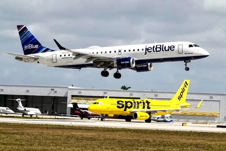 A JetBlue airliner lands past a Spirit Airlines jet on taxi way at Fort Lauderdale Hollywood International Airport on April 25, 2022, in Florida.