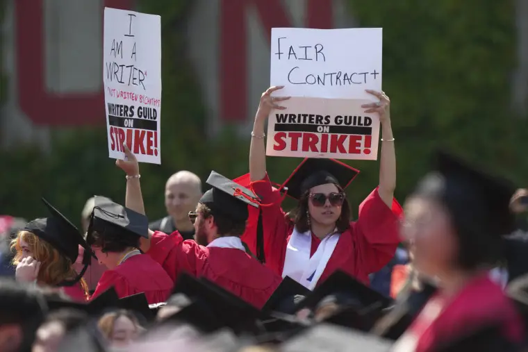 Graduating students hold signs in support of the Hollywood writers' strike during David Zaslav's commencement address